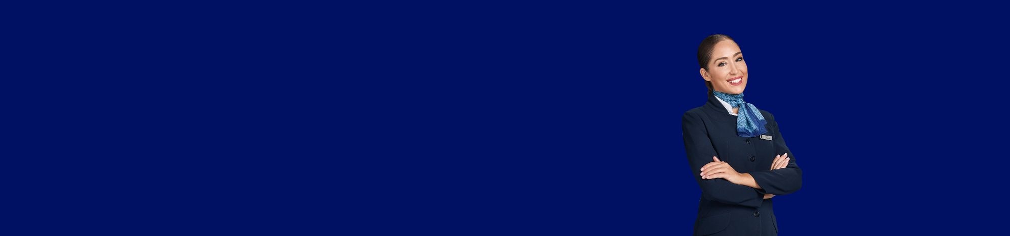 Asistente de vuelo sonríe con brazos cruzados, fondo azul sencillo.