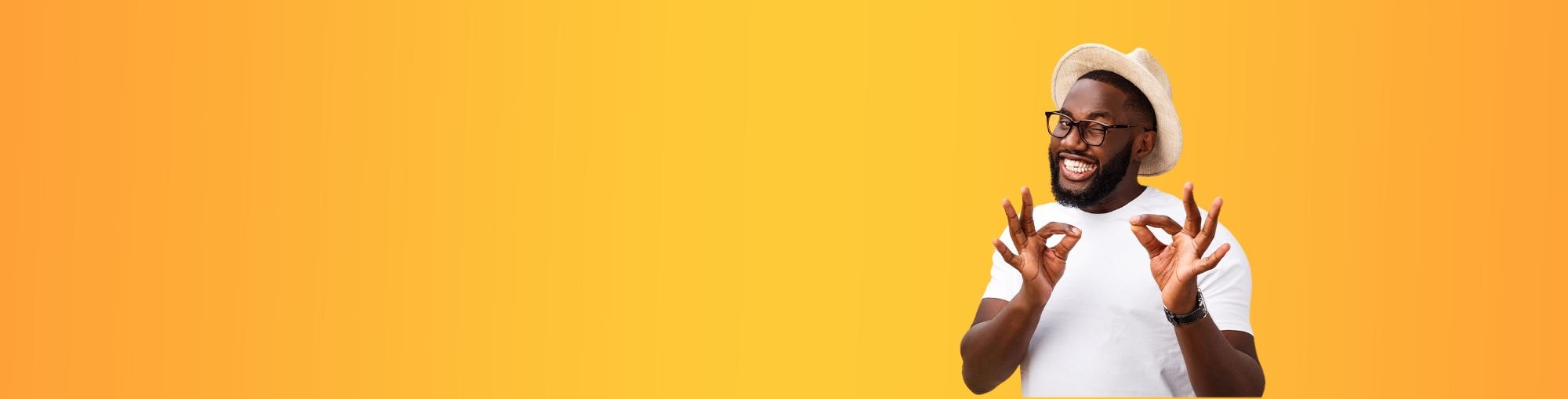 Hombre sonriente haciendo gestos con manos, fondo amarillo uniforme. Lleva sombrero y gafas.