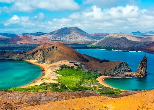 A volcanic mountain rises above turquoise seas in an island landscape with sparse vegetation.
