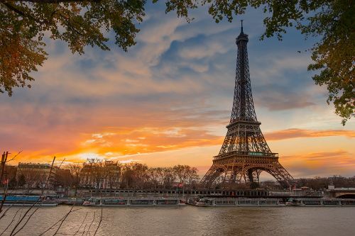 Torre Eiffel al atardecer, junto al río, rodeada de árboles y edificios.
