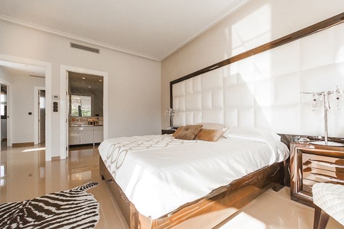 Cama moderna con cabecero acolchado en habitación luminosa; alfombra animal print y mesitas elegantes.