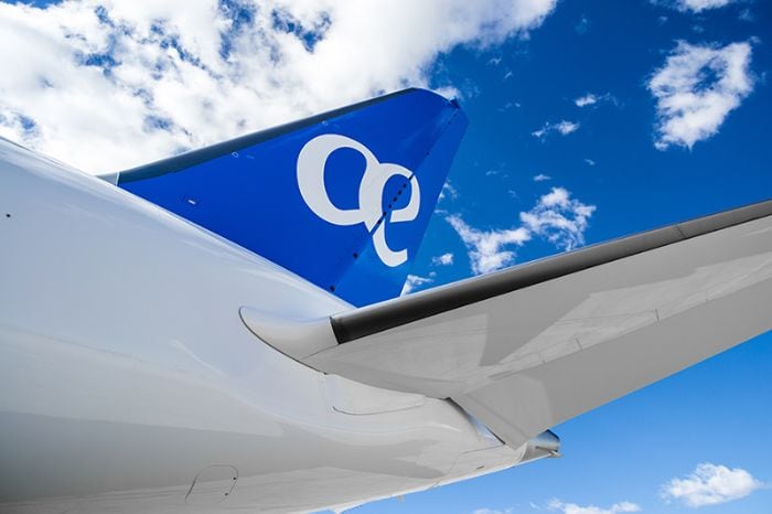Cola de avión azul con logo "oe" en un cielo despejado con nubes blancas.