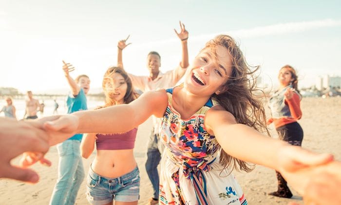 Grupo de jóvenes sonrientes bailando juntos en la playa durante una tarde soleada.