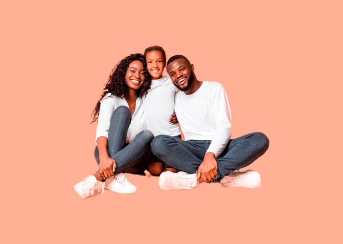 Three people smile while sitting on the floor against an orange background, wearing casual white clothing.