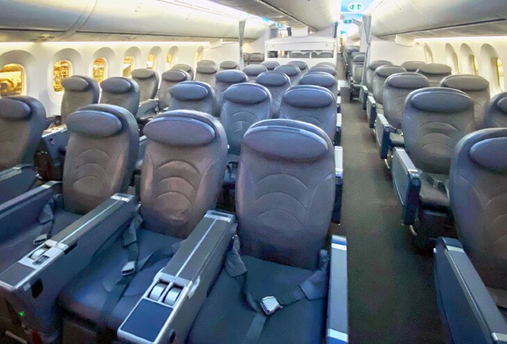 Asientos vacíos alineados, dispuestos en filas, dentro de la cabina de un avión iluminado.